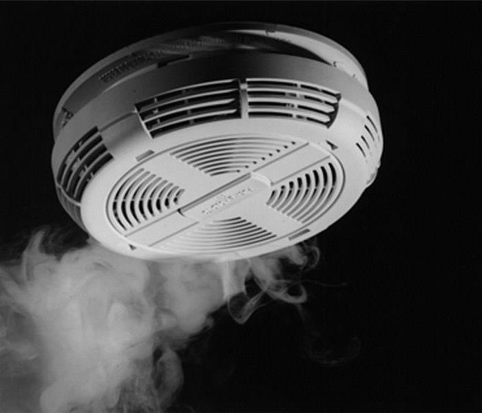 Smoke detector on ceiling with smoke rising around it