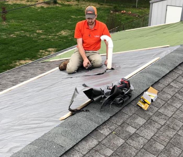 employee in an orange shirt tarping a roof 
